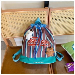 Close-up of striped canvas drawstring backpack with cute plush bear charms on a chair