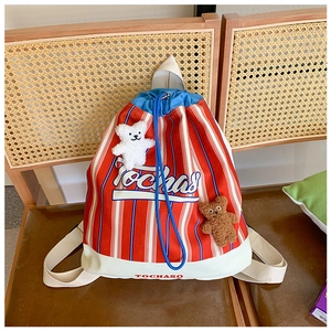 Detail of red striped canvas drawstring backpack with two plush bear charms on chair