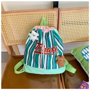 Detail of green striped drawstring backpack for kids featuring a plush bear charm on a chair