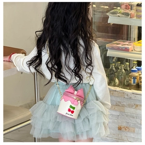 Détail du sac seau enfant avec nœud rose, imprimé cerise et chaîne dorée