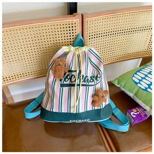 Detailed view of canvas drawstring backpack with colorful stripes and plush bear charms