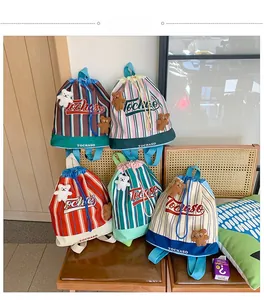 Close-up of assorted striped drawstring backpacks with plush bear charms on a wooden chair