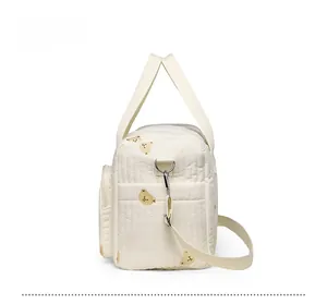 Side view of cream quilted diaper bag featuring cute bear print and adjustable strap