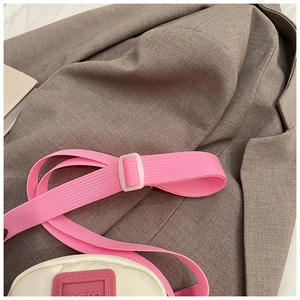 Detail of white mini shoulder bag showing pink nylon strap and square rubber logo patch