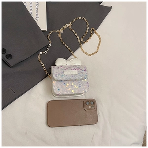 Detail of a mini sequin crossbody bag with a large white bow and golden metal chain