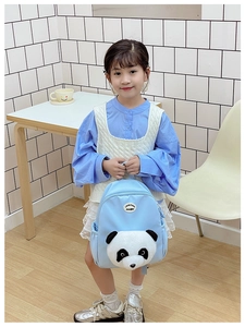 Young girl wearing a light blue panda backpack with plush 3D panda head in a cozy room