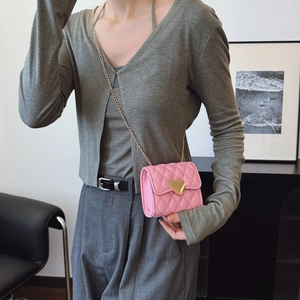 Pink quilted girls crossbody bag with gold heart clasp and chain strap modeled in a room