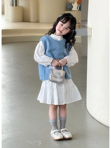 Détail du gilet en tricot bleu clair et robe à manches bouffantes blanche avec sac argenté