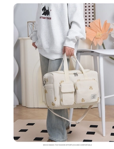 Quilted beige diaper bag with bear embroidery, showing side pockets and shoulder strap