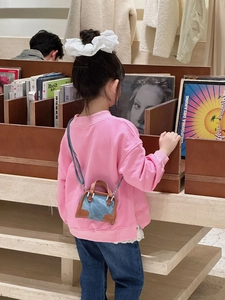 Tout-petit en sweat rose portant un mini sac bandoulière en denim bleu et cuir marron