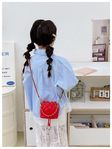 Détail d'un sac seau matelassé rouge pour enfant avec chaîne dorée porté par un modèle