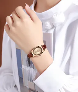 Gros plan d'une montre à quartz ovale dorée avec bracelet en cuir marron au poignet