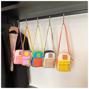 Detail of five colorful mini canvas crossbody bags hanging on a sleek metal rack