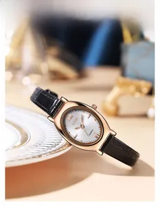 Détail d'une montre ovale en or rose avec cadran rayonnant et bracelet en cuir noir fin