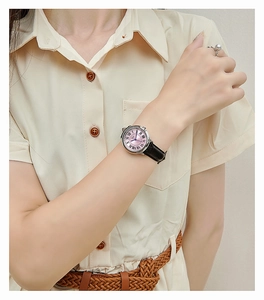 Classic women's quartz watch with pink dial and black leather strap worn on wrist