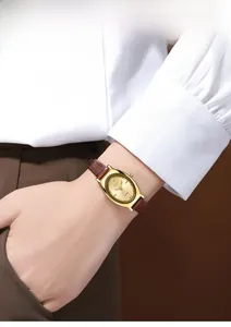 Gros plan d'une montre à quartz ovale dorée avec bracelet en cuir marron au poignet