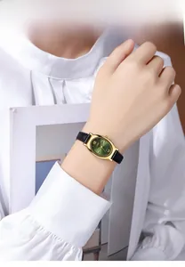 Gros plan d'une montre ovale dorée avec cadran vert et bracelet en cuir noir au poignet