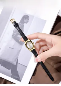 Détail d'une montre à quartz ovale dorée avec un bracelet en cuir noir texturé