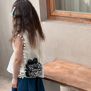Kids sequin shoulder bag in black with bow detail and gold chain strap worn by child