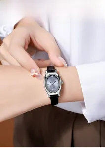 Montre à quartz ovale avec cadran gris et bracelet en cuir noir portée par une femme