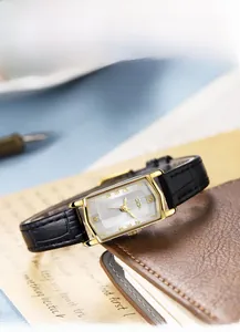 Detail of vintage rectangular quartz watch with gold case and black leather strap on desk