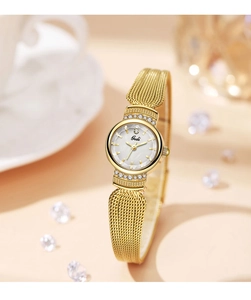 Détail d'une montre dorée à mailles milanaises avec lunette sertie sur fond de tons chauds