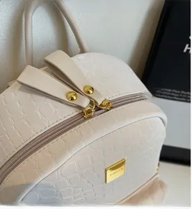 Close-up of cream crocodile pattern backpack with gold dual zippers and metal brand plate