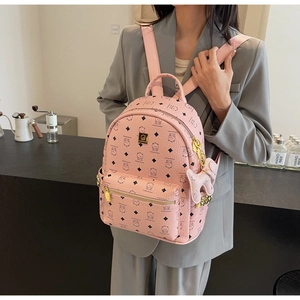 Pink leather backpack with bear pattern print and cute dog charm shown in a cafe