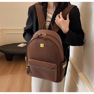 Detail of dark brown woven texture backpack with gold logo plate and side stud accents