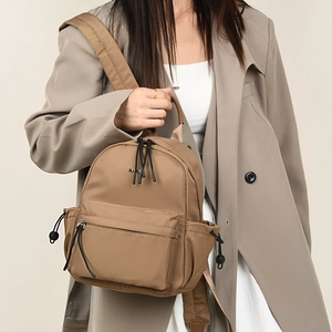 Detail of khaki nylon backpack featuring YSOL metal logo and functional front zipper pocket
