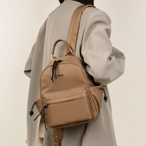Detail view of khaki travel backpack with drawstring side pockets and metal logo