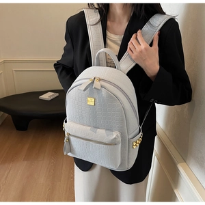 Detail of grey crocodile embossed leather backpack with gold rivets and metallic logo