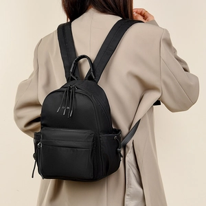 Close-up of minimalist black nylon travel backpack showing white letter logo and zipper detail