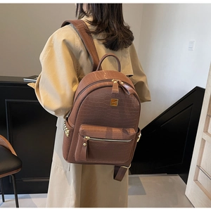 Detail of brown crocodile pattern backpack featuring side gold studs and metal brand plate