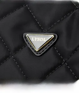 Gros plan sur la texture en nylon matelassé noir et le logo métallique sur le sac bandoulière