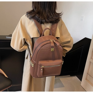 Brown crocodile embossed leather backpack with gold rivets worn by a model on a trench coat