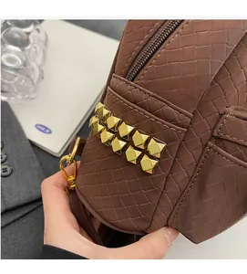 Detailed close-up of brown woven texture bag featuring golden pyramid rivets and hardware
