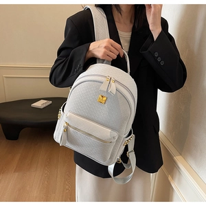 Detail of white woven texture backpack with gold logo plate and rivet accents