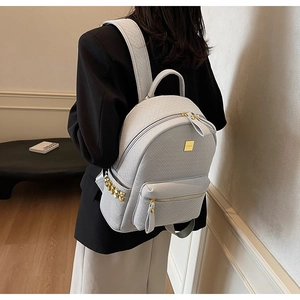 Close-up of light gray woven texture backpack with gold metallic studs and logo plate