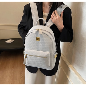 Detail of woven texture backpack featuring gold logo plate and side rivet accents