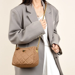 Détail du sac bandoulière matelassé marron avec chaîne dorée sur un blazer gris