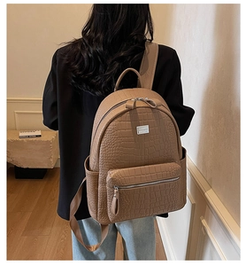 Detail view of khaki faux leather backpack with embossed crocodile texture and metal logo