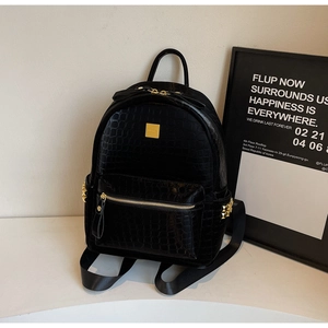 Close-up of black croc-embossed backpack with gold metal zippers and rivet details