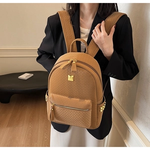 Detail of khaki woven backpack with gold logo plate and side metallic cone studs