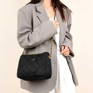 Détail du sac matelassé noir avec chaîne dorée et emblème triangulaire sur blazer gris