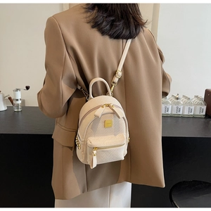 Detail of a beige mini backpack with quilted texture and gold hardware on a model