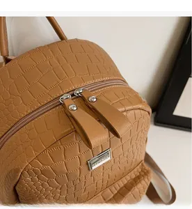 Close-up of smooth double zippers and crocodile embossed leather on brown backpack