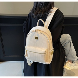 Detail of cream-white woven backpack with gold hardware and zipper, shown on model