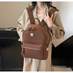 Detail of brown quilted backpack featuring gold metal logo and front zipper pocket