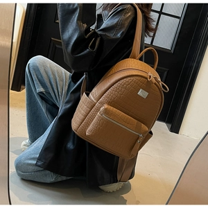 Detailed side view of brown crocodile embossed leather backpack worn by a model